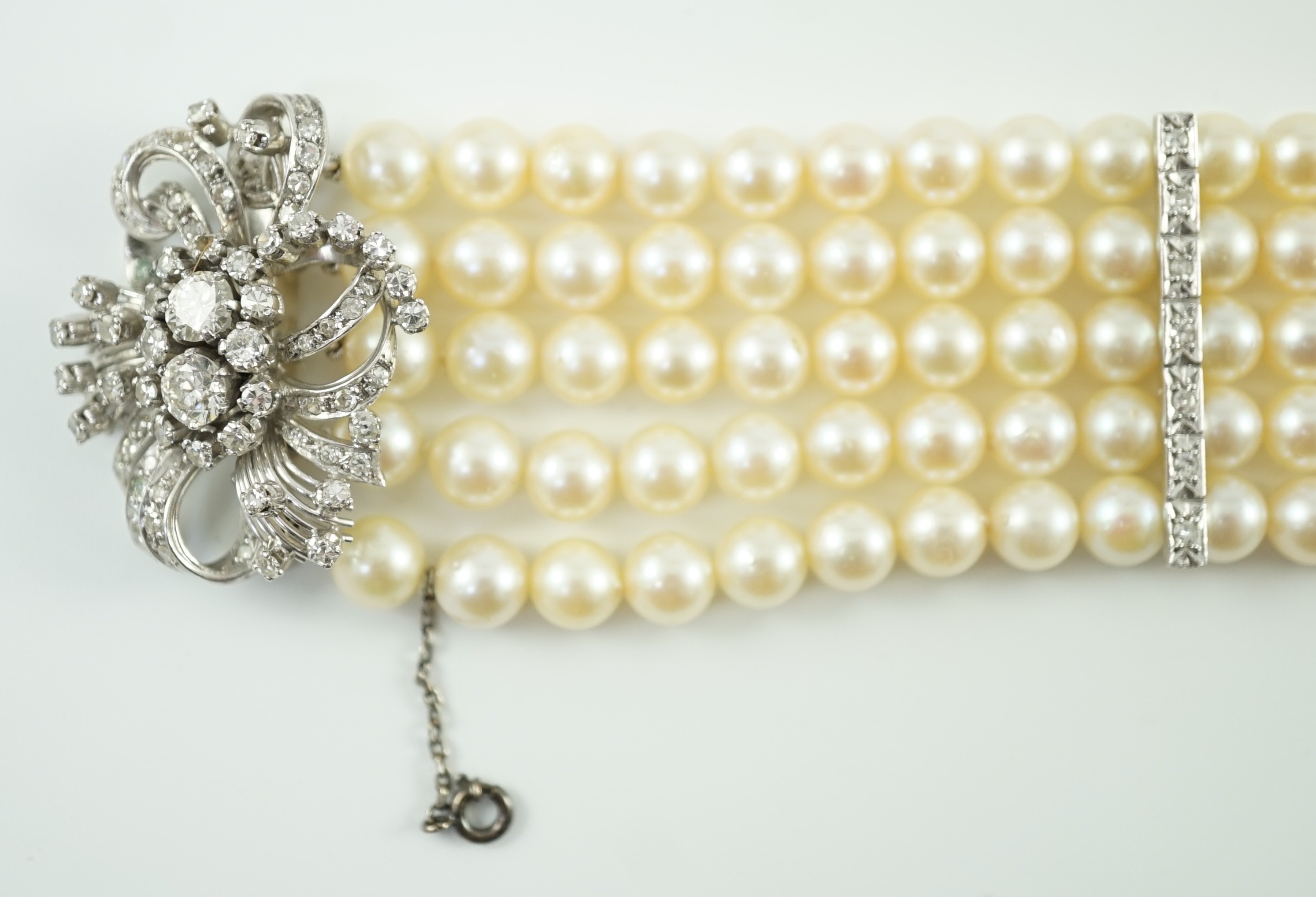 A mid to late 20th century continental quintuple strand cultured pearl bracelet, with white gold and diamond cluster set scroll clasp and diamond set line spacers